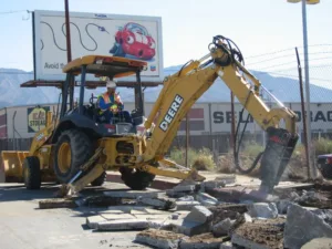 hydraulic breaker mounted on backhoe being used to demo concrete sidewalk